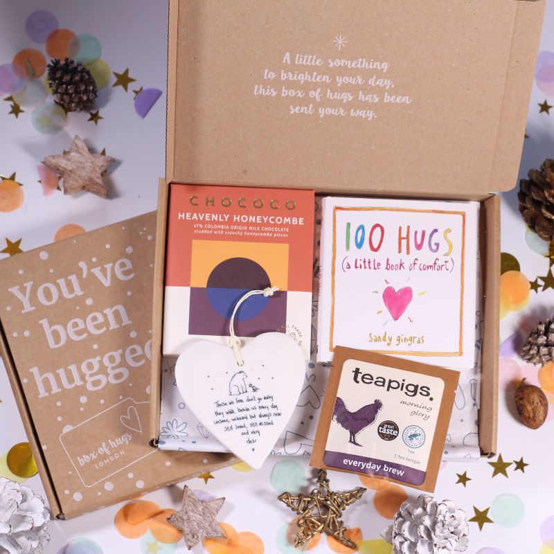 Gift box with 'You've been hugged' card, '100 Hugs' book, and 'Chocola Heavenly Honeycombe' product on a decorative background.