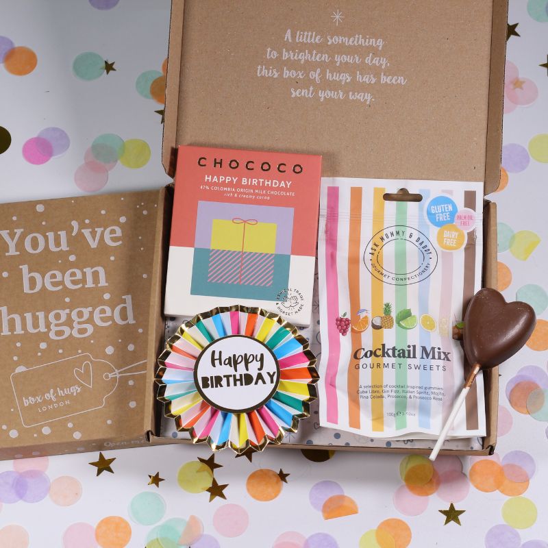 Open box of 'Box of Hugs' with birthday-themed items on a colorful confetti background