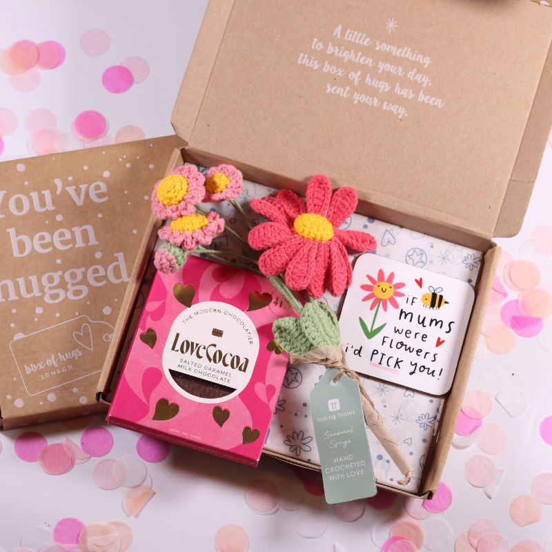 Gift box with flowers, chocolate, and a card on a pink and white background