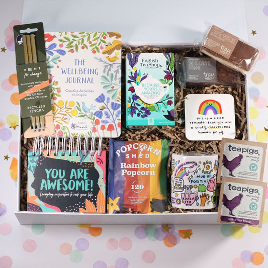 Assorted items including a journal, tea bags, and snacks in a box with a colorful polka dot background.