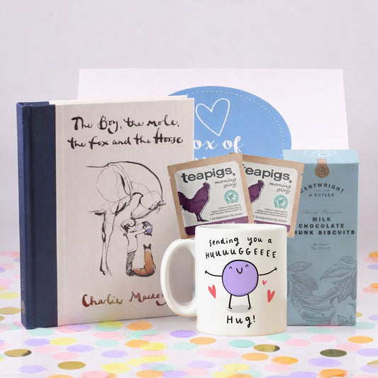 Gift set with a The Boy the mole the fox and the horse book, mug, teapigs tea packages, and chocolate bars on a colorful polka dot surface.