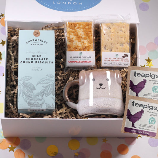 Gift box with a dog mug, chocolate chunk biscuits, teapigs tea sachets, shortbread and a flapjack on a colorful background