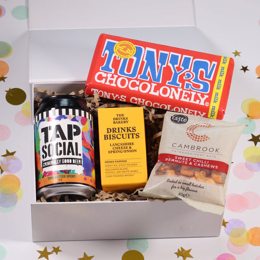 A gift box with an assortment of items including a beer can, a chocolate bar, cheese biscuits, peanuts and cashews,