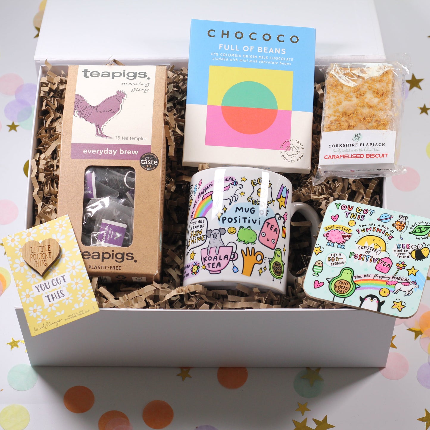 Gift box with tea, snacks, and a mug on a light background
