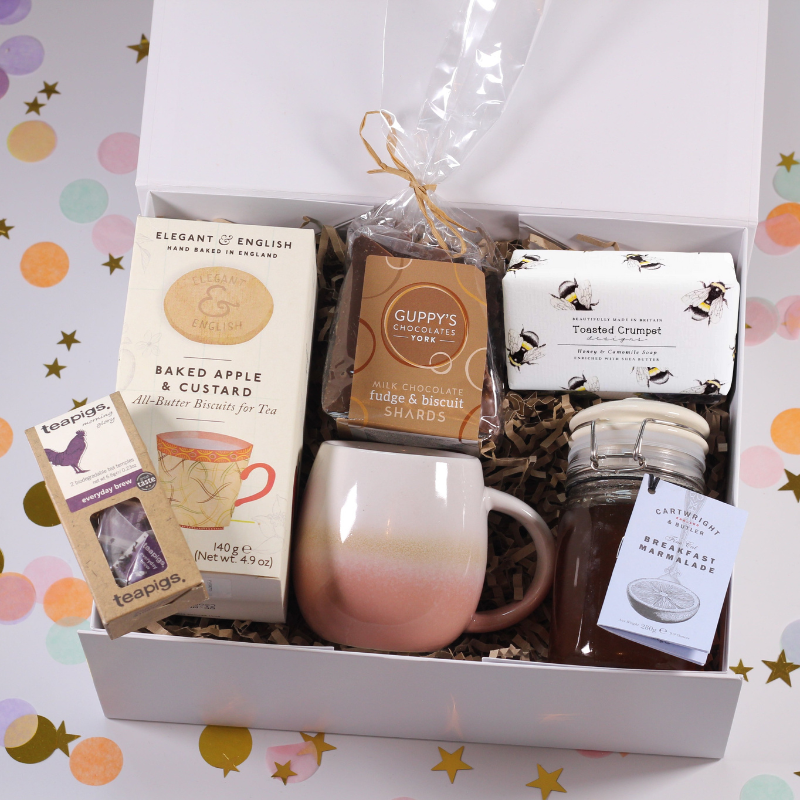 Gift basket with a mug, tea, biscuits, jam and soap on a colorful background