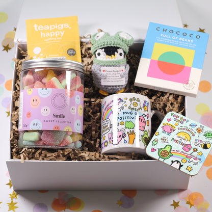 Gift box with various items including a penguin plush toy, a jar of gummy bears, and a card on a decorative background.