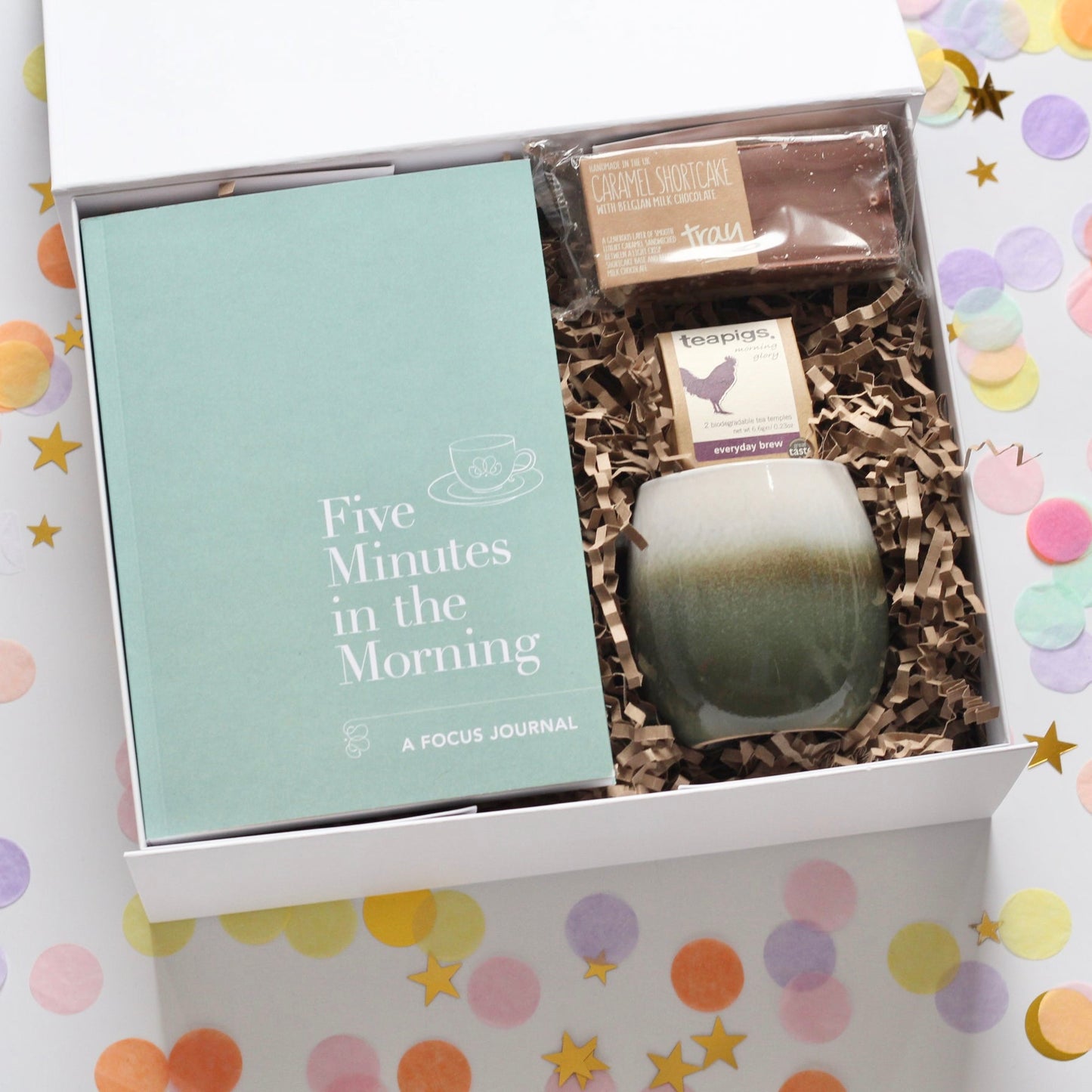 A gift box set containing a green ombre mug, a focus journal, a caramel shortcake with Belgian chocolate, and a card for a personalized message.