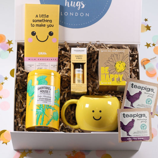 Box of Hugs Gift box  with a yellow happy mug, tea, be happy grow your own sunflowers, smile chocolate  and lemon biscuits on a colorful background