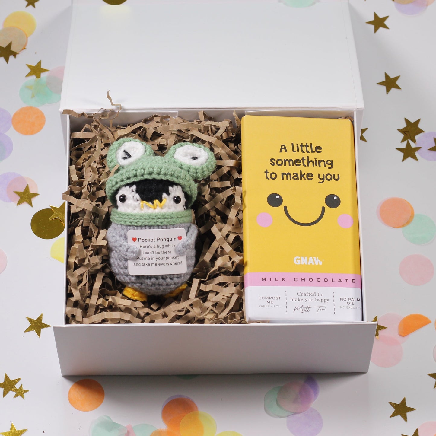 Gift box with a crocheted penguin toy and a chocolate bar on a colorful background