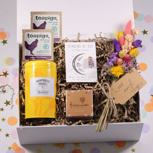 Gift box with tea, lemon biscuits, thinking of you crystals, chocolate truffles, and dried flowers on a colorful background