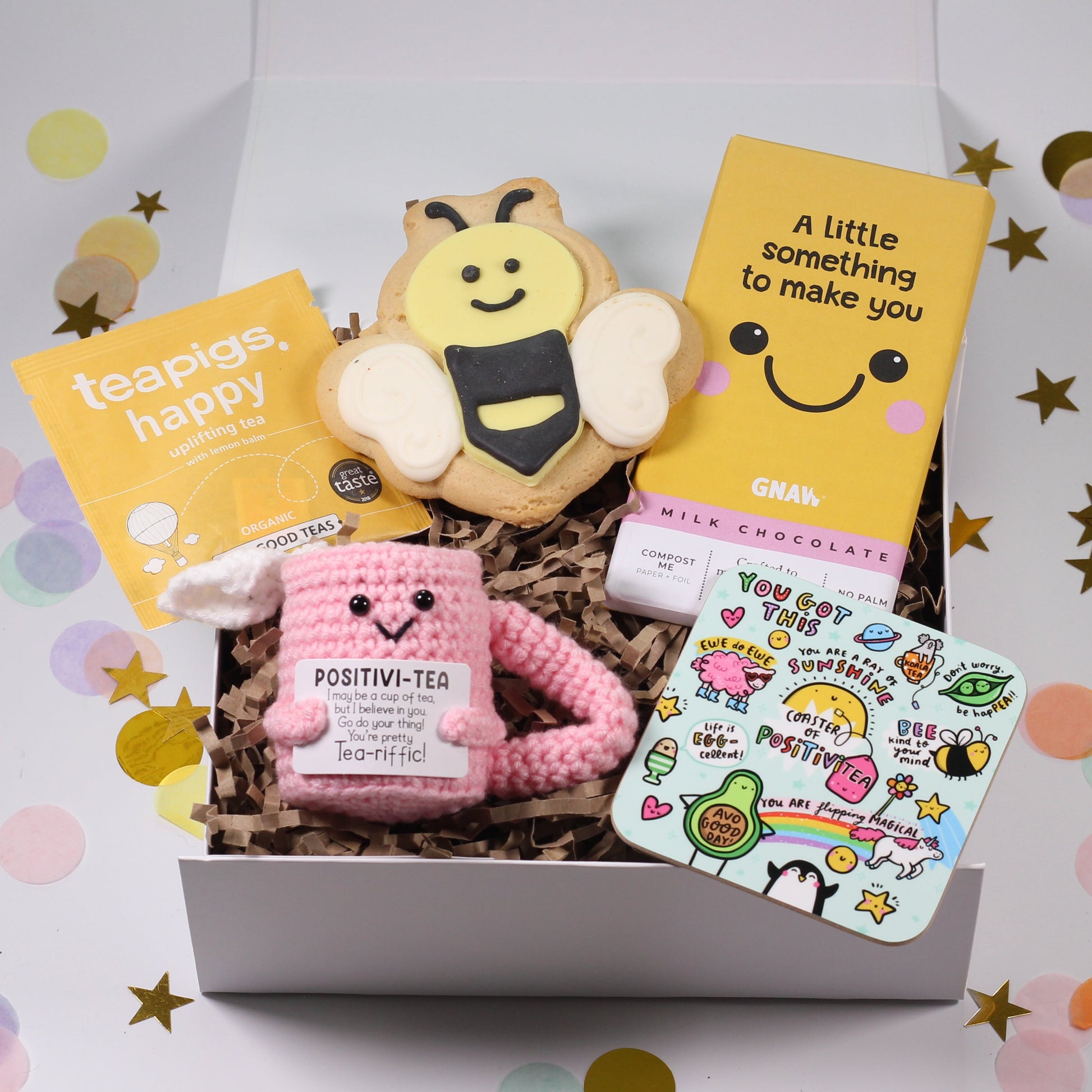 Gift box with an iced bee biscuit, a positivi-tea crochet cup with uplifting quote, a positivi-tea coaster, smile chocolate bar on a confetti background