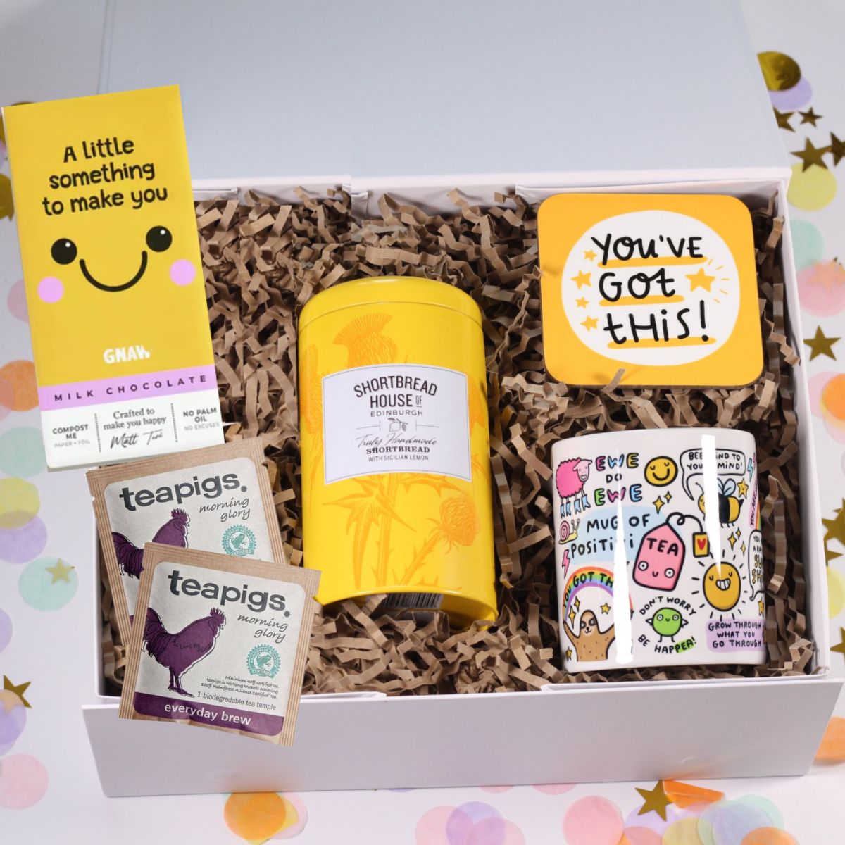 Gift box with a positive mug, teapigs tea bags, you've got this coaster, lemon shortbread on a colourful background.