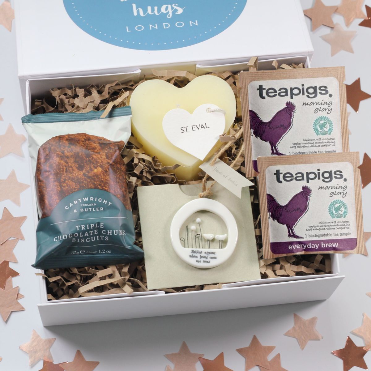 Gift box with tea, heart candle, triple chocolate chunk biscuits, robins appear when loved ones are near hanging sign, on a star-patterned background