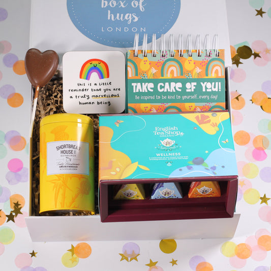 A gift box with various items including a card, a perpetual calendar, an uplifting coaster, lemon shortbread biscuits, wellness tea and a chocolate lollipop.