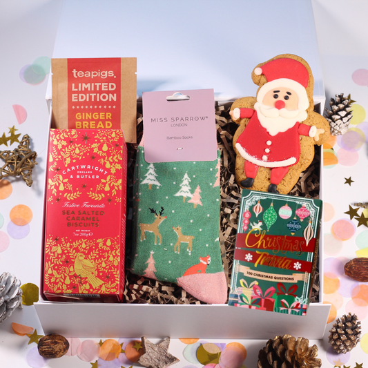 Christmas-themed gift box with Christmas themed socks, a Santa Claus cookie,  Christmas Trivia cards, and sea salted and caramel biscuits.