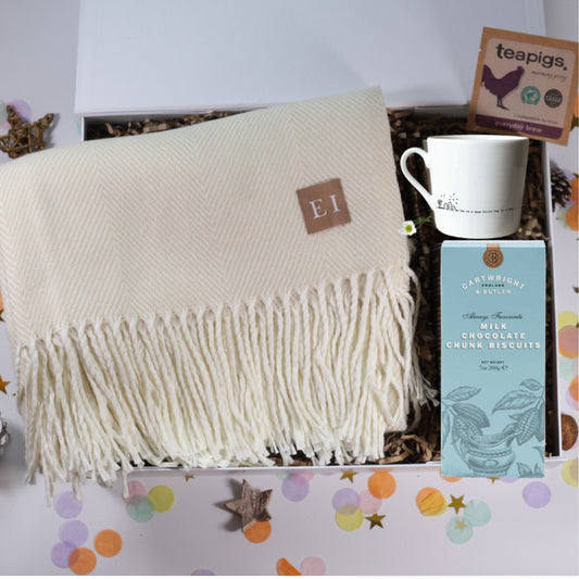 White throw blanket with fringe, mug, and box of biscuits on a decorative surface