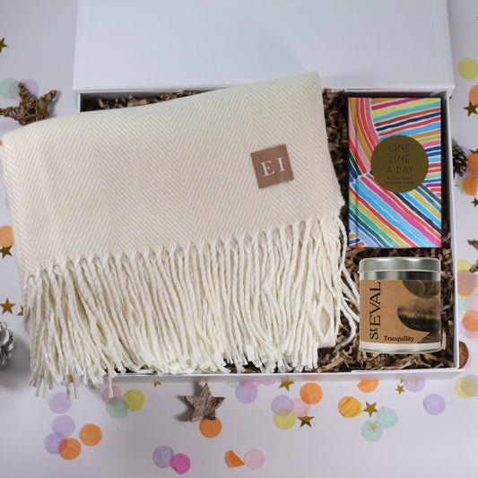 Gift box with a white blanket, candle, and colorful one line a day journal book inside.