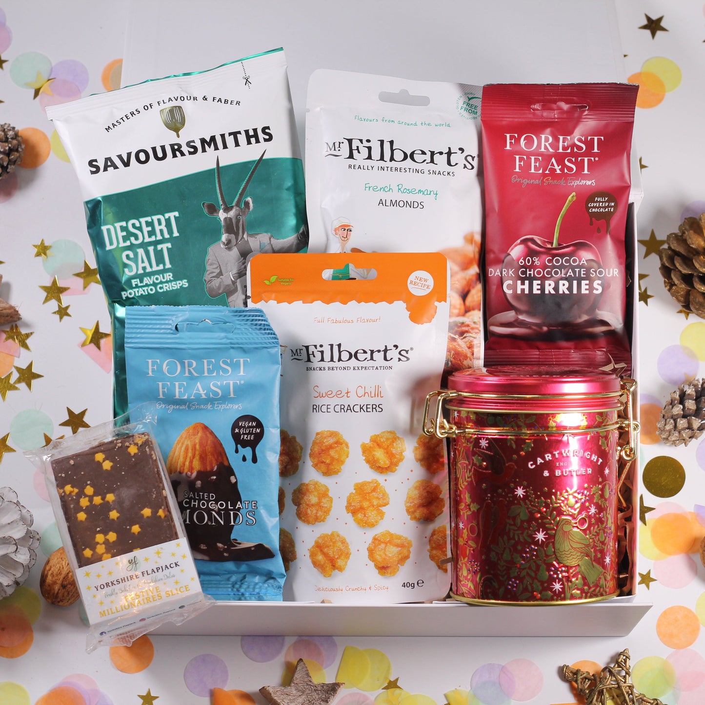 Christmas gift box with Assorted christmas snacks including Christmas tin of fudge, Savoursmiths crisps, Mr Filbert's almonds amd chilli crackers, and Forest Feast chocolate almonds and cherries and festive flapjack.
