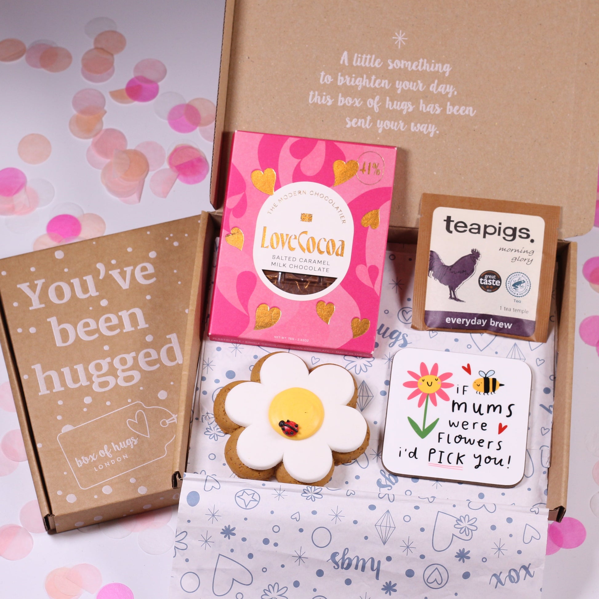 Gift box with 'if mums were flowers id pick you coaster, flower cookie, chocoalte and tea on a pink confetti background.