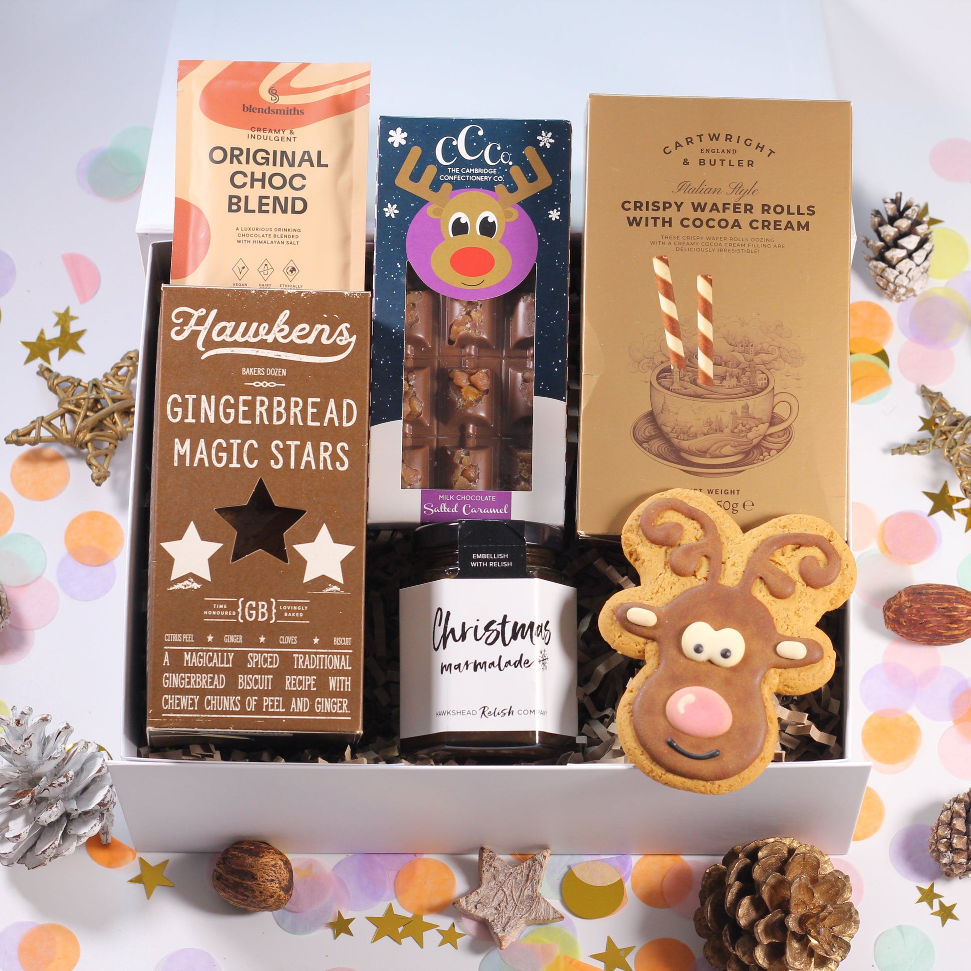Christmas gift box with Assorted Christmas-themed treats including gingerbread stars, Christmas marmalade, rudolph chocolate bar, crispy wafer rolls, hot chocolate and iced gingerbread biscuits.