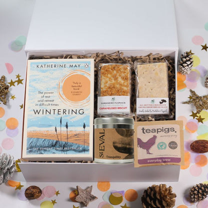 Gift box with the Wintering book by Katherine May, St Eval Tranquility tinned candle and some flapjack and shortbread, on a decorative background