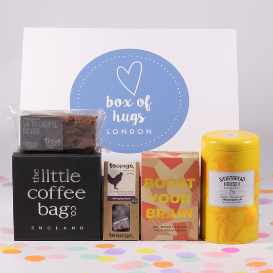 A collection of gift items including a 'Boost Your Brain' puzzle book, shortbread biscuits with Sicilian lemon, a salted caramel brownie, a little coffee bag co taster box, and a 'Box of Hugs' card.